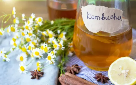 Bouteille de kombucha ambré, décorée de camomille, d'anis étoilé, de bâtons de cannelle et d'une tranche de citron.