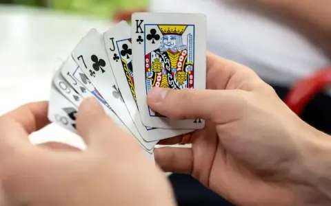 Dłonie trzymają karty do gry. Widać figury: króla, waleta i damę.