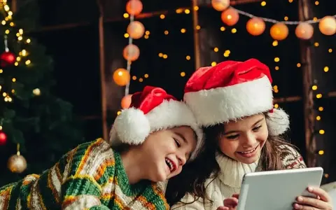 Dos niños con gorros de Santa Claus disfrutan de la tablet, felices cuando dan vacaciones de Navidad, rodeados de luces festivas y un árbol.