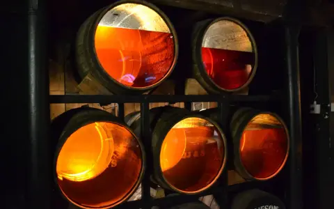 Drewniane beczki z bursztynowym whisky, część trunku to whisky angel share, dojrzewająca w ciemnej piwnicy.