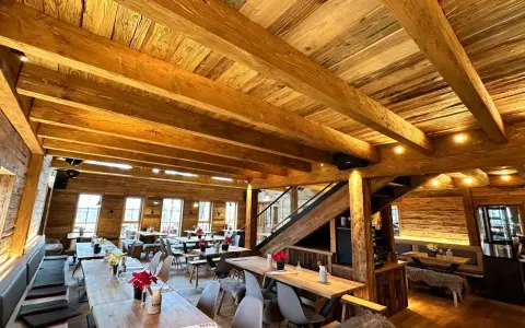 Gemütliches Holzinterieur eines Restaurants mit Holzbalken und Tischen.
