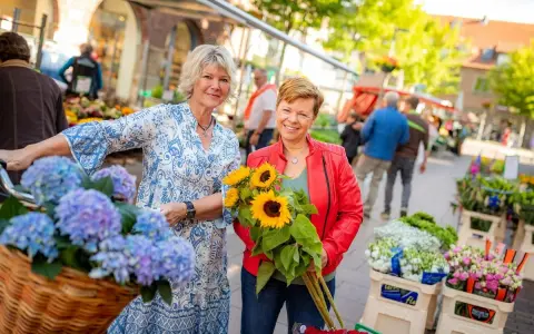 Zwei Frauen mit Blumen auf dem Markt in Coesfeld. Eine hält Sonnenblumen, die andere hat Hortensien im Fahrradkorb.