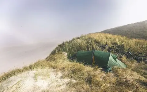 Grön tält och cyklar på en gräsbevuxen sanddyn vid havet. En idyllisk plats för äventyr i sanddynerna Danmark.