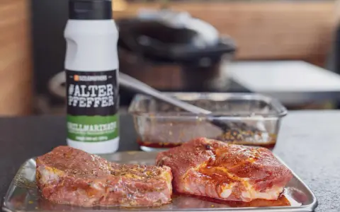 Zwei Steaks liegen auf einem Blech, bereit für die beste Steak Marinade. Daneben eine Flasche "#ALTER PFEPPER" Grillmarinade.