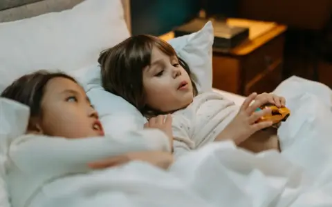 Dos niños en la cama, uno con un coche de juguete, quizás planeando travesuras o contando mentiras en niños de 10 a 12 años.