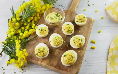 Œufs mimosa garnis d'une sauce crémeuse et de ciboulette, présentés sur une planche en bois avec des fleurs de mimosa. Une recette printanière.