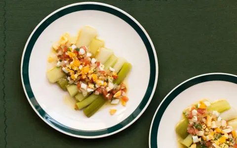 Puerros a la vinagreta servidos en platos blancos con borde verde, cubiertos con una mezcla de tomate picado, huevo duro y perejil.