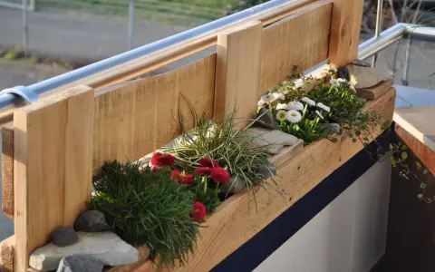 Balconi fioriti moderni con vasi in legno grezzo, margherite bianche e rosse, erba ornamentale e pietre.