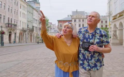 Starsze małżeństwo odkrywa urokliwe, przyjazne seniorom miasta. Kobieta z aparatem wskazuje na zabytkową architekturę.