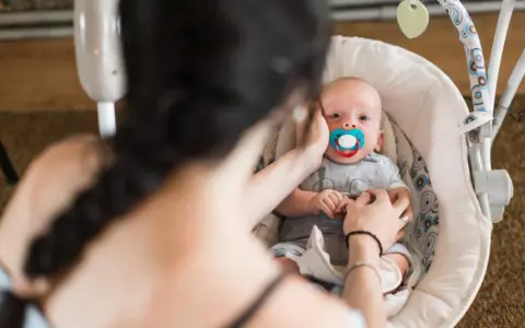 Maluszek w bujaczku polecanym przez fizjoterapeutów. Mama delikatnie głaszcze go po główce, uspokajając.