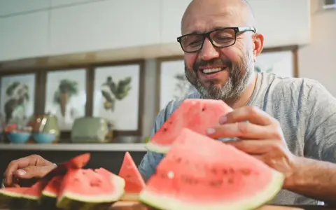 Glücklicher Mann mit Brille isst Wassermelone. Die Wassermelone Nachteile sind, dass sie schnell aufgebraucht ist.
