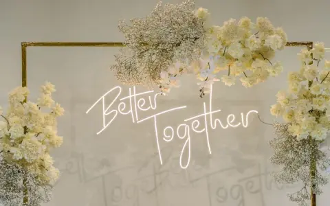 Elegancka ściana z kwiatów w kremowych odcieniach, ozdobiona neonowym napisem "Better Together".
