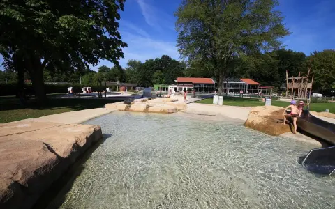 Kinder planschen im flachen Wasser des Parkbad Versmold. Eine Rutsche lockt zum Spielen.