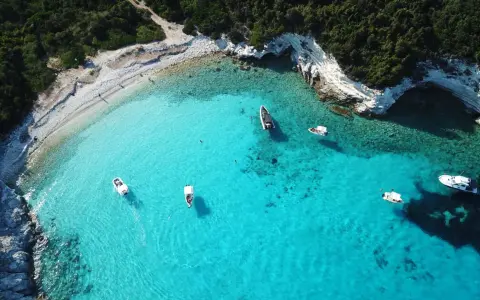 Idealne wakacje na Paxos: turkusowa woda, białe skały i łodzie unoszące się na falach.
