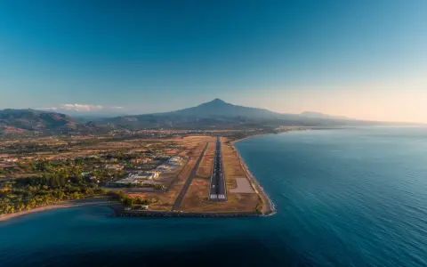 Flygplats vid havet med berg i bakgrunden. En landningsbana sträcker sig ut mot vattnet, en vy som påminner om Palermo flygplats.