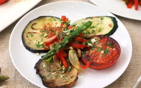 Deliciosa parrillada de verduras con berenjena, calabacín, tomate, pimientos y espárragos, todo aderezado con ajo y perejil.