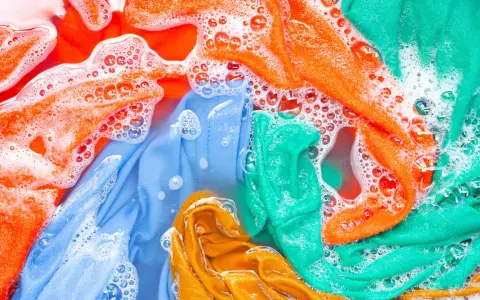 Ropa de color lavadora con burbujas de jabón. Prendas naranjas, azules, verdes y amarillas sumergidas en agua.