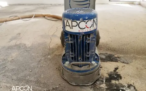Maszyna APCON przygotowuje podłoże pod parkiet, szlifując beton. Wąż odkurzacza leży obok.