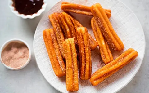 Churros sin gluten espolvoreados con azúcar y canela, servidos con chocolate caliente.
