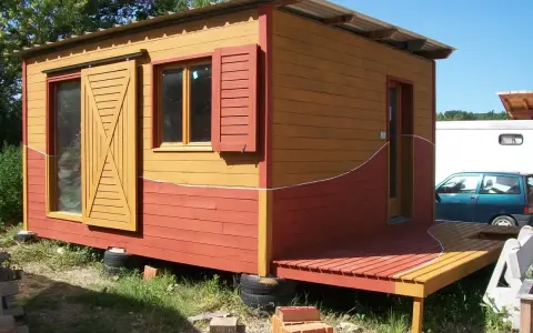 Maisonnette en bois aux couleurs vives, rappelant un nuancier peinture suédois. Porte coulissante jaune, volets rouges.