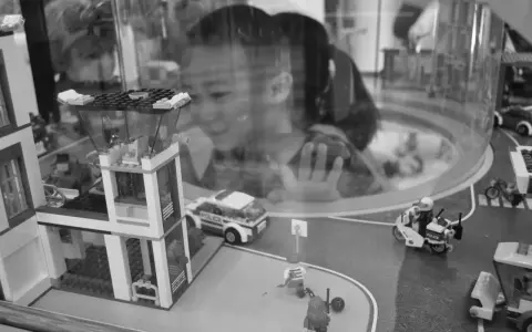 Bambina osserva con stupore un **reportage fotografico** di idee con costruzioni Lego: un commissariato, auto della polizia e personaggi in azione.