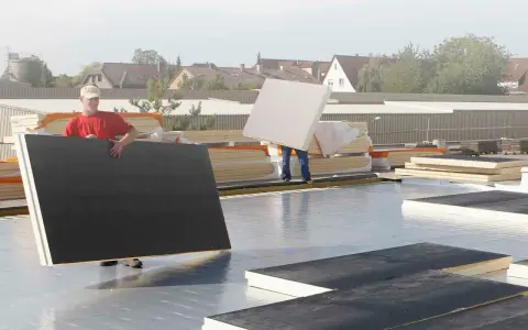 Arbeiter verlegen Dämmplatten auf einem Dach. Die Platten entsprechen der DIN 18234 und werden für die Dachisolierung verwendet.