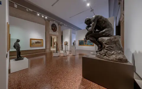 Il Pensatore di Rodin domina la sala del museo Ca' Pesaro, circondato da altre sculture e dipinti.