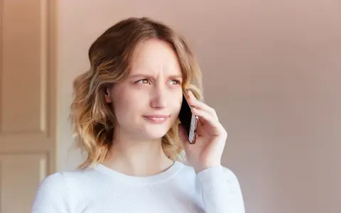 Zmarszczona kobieta rozmawia przez telefon, próbując dowiedzieć się, jak zwiększyć głośność w telefonie, bo rozmówca mówi za cicho.