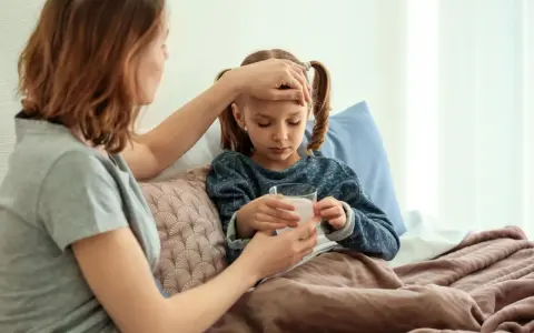 Mutter prüft Fieber bei krankem Kind im Bett. Die Krankschreibung für die Schule ist nötig, damit das Kind sich erholen kann.