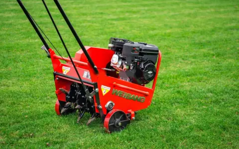 Czerwony aerator WEIBANG na zielonej trawie, gotowy do pracy. To urządzenie zapewnia doskonałą aerację trawnika, poprawiając jego wygląd i zdrowie.