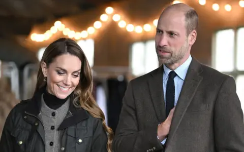 Prins William av Wales och Kate Middleton ler under en ljusslinga.