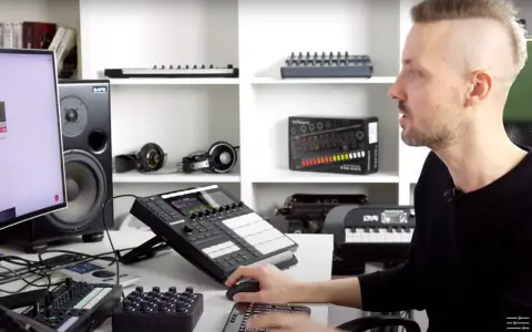 Mężczyzna uczy się produkcji muzyki przy komputerze, otoczony sprzętem: kontrolerami, głośnikami i słuchawkami.