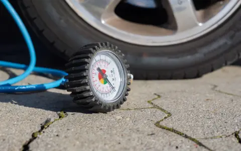 Manomètre de pression des pneus à côté d'une roue de voiture et d'un tuyau bleu.