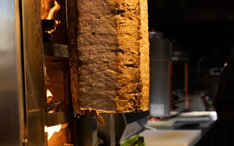 Duży pionowy obrotowy grill z mięsem, obok płomienie ognia.