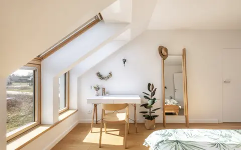 Angolo studio mansardato inondato da la luce più naturale. Scrivania, sedia in legno, specchio alto e pianta.