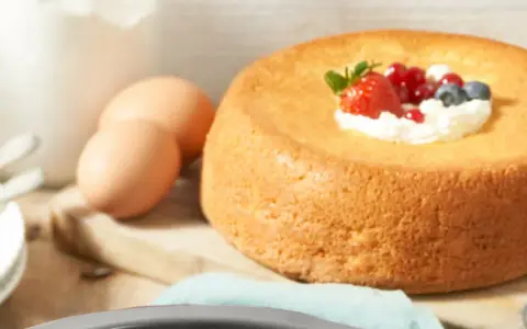 Un savarin traditionnel, doré et moelleux, garni de crème fouettée et de fruits rouges. Des œufs et de la farine sont prêts pour la préparation.