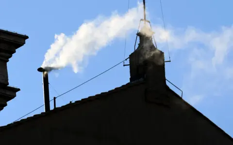 Biały dym z komina, jak sygnał wyboru nowego papieża, unosi się na tle błękitnego nieba.
