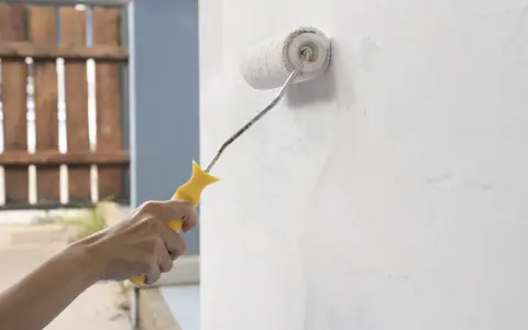 Mano aplicando imprimación a paredes con rodillo. Preparando la superficie para pintar.