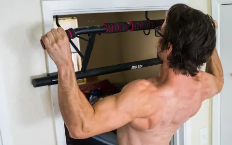 Homme musclé s'entraînant avec une barre de tirage porte d'entrée. Avis : installation facile et solide pour un entraînement efficace.