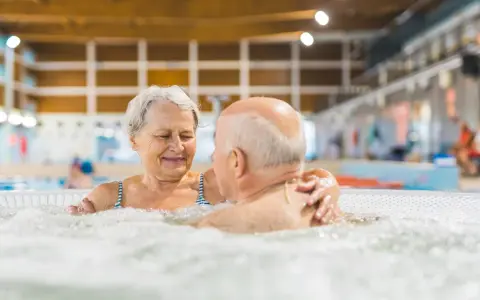 Uśmiechnięta para seniorów relaksuje się w jacuzzi w basenie. To wspaniałe miejsce, jak sanatorium szpitalne, gdzie można odzyskać siły.