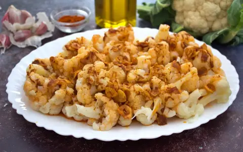 Coliflor al ajillo servida en un plato blanco, con ajo laminado y pimentón espolvoreado.