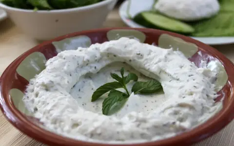 Kremowy labneh co to? Gęsty, biały serek z ziołami, udekorowany świeżą miętą, w glinianej misce.