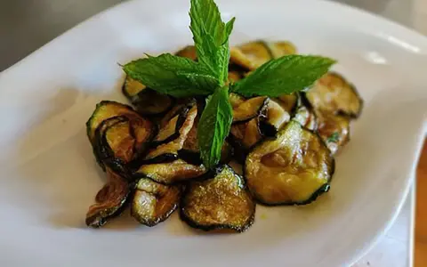 Zucchine alla scapece dorate e croccanti, guarnite con foglie di menta fresca, servite su un piatto bianco.