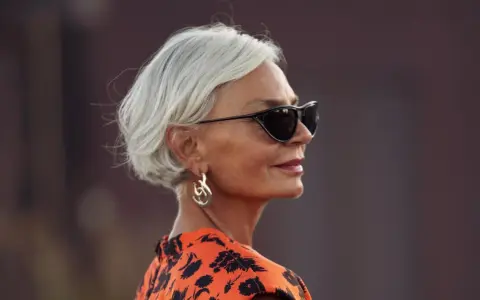 Elegante Frau mit Kurzhaarfrisur ab 60, Sonnenbrille und auffälligem Ohrring.