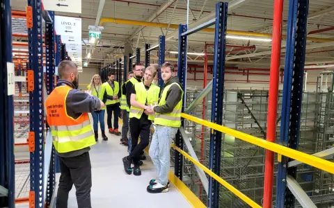 Grupa osób w kamizelkach odblaskowych zwiedza magazyn CEVA Logistics. To potencjalna ceva logistics praca.