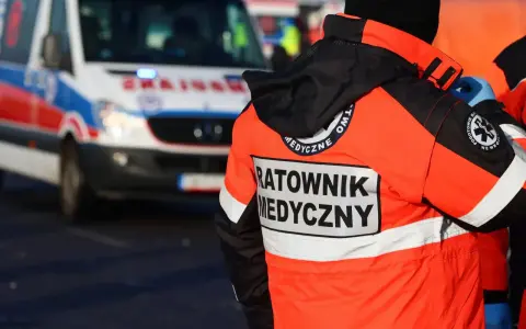Ratownik medyczny w jaskrawej kurtce stoi obok karetki pogotowia.