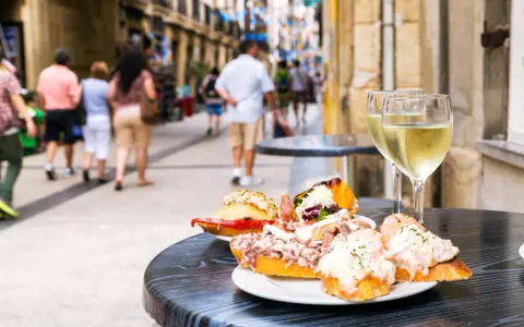 Tapas och vin på en uteservering i San Sebastián. Folk promenerar förbi på den livliga gatan.