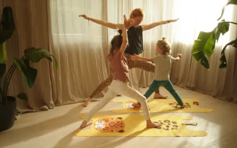 Eine Frau und zwei Kinder üben Yoga auf bunten Matten. Die Kinder haben Spaß bei den Yoga-Übungen.