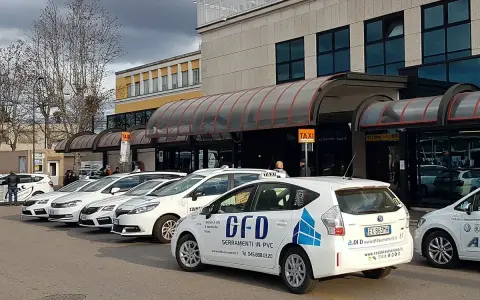 Reihe weißer Taxis vor einem Gebäude mit Taxischildern.