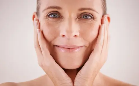 Visage d'une femme aux mains sur les joues, montrant les signes du temps et les défis des problèmes de peau et ménopause.